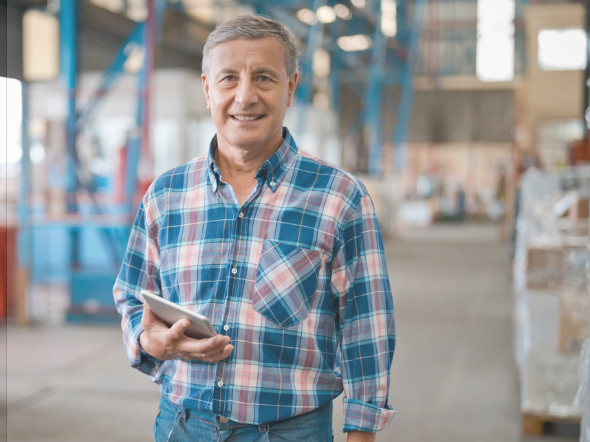 Mature male manager in warehouse smiling at camera wearing a flannelette shirt