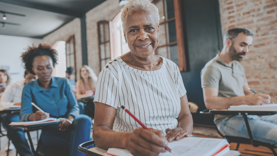 A closeup of a matured aged smiling at the camera sitting in her diverse classroom of peers