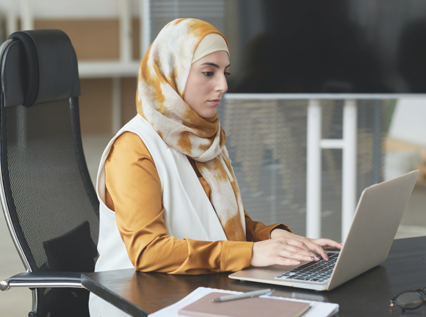 Portrait of female wearing hijab sitting at a computer desk studying. 