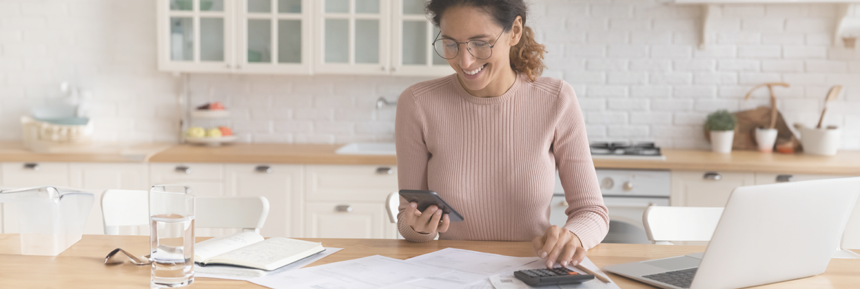 Young 30s Latina woman sitting at kitchen counter working out EST Course payments. 