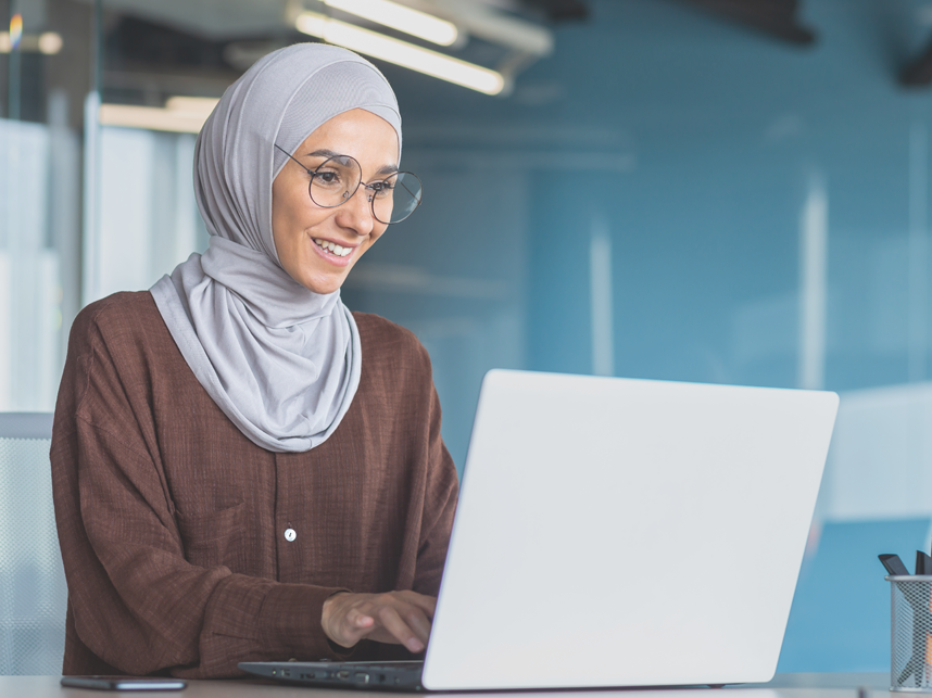 Woman wearing a hijab working on finance documents on  her laptop.