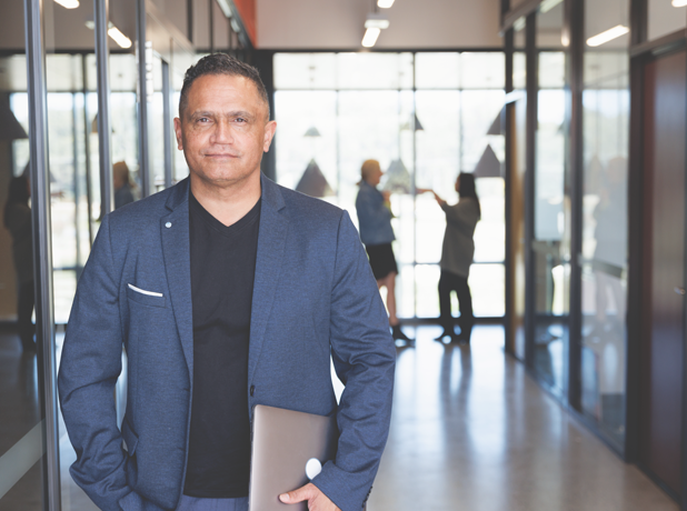 Man in a navy blazer holding laptop and looking at the camera.