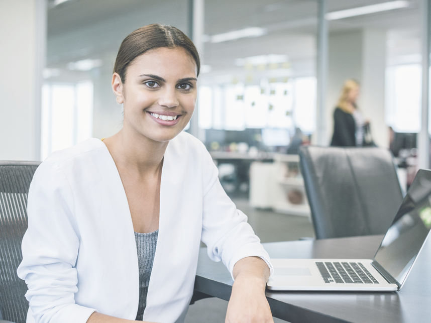 Business woman at desk looking at the camera and smiling.