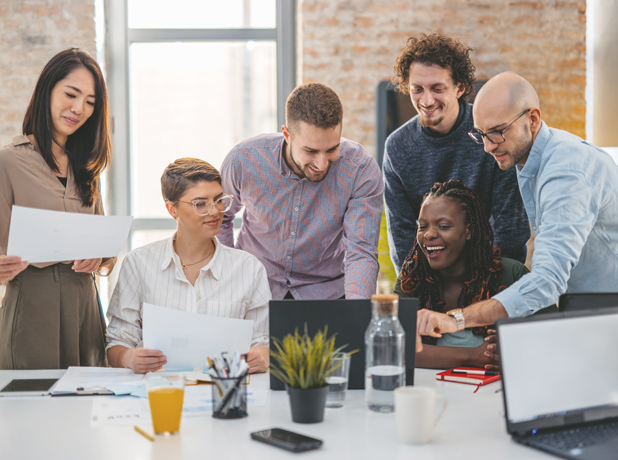 A diverse business team crowd around a laptop cheerfully working together on a project