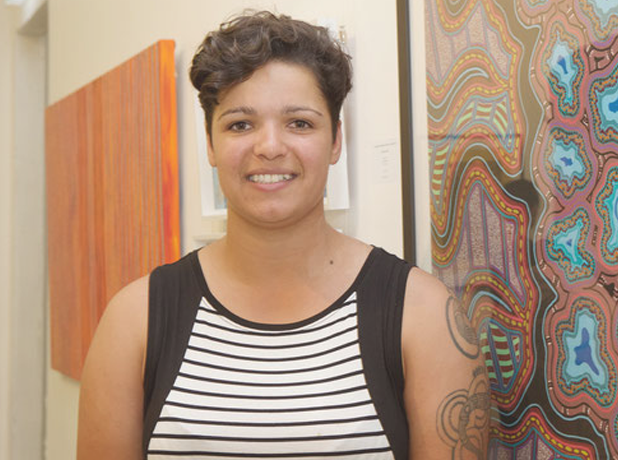 Artist Jasmine Sarin facing forward smiling in front of an Aboriginal Artwork