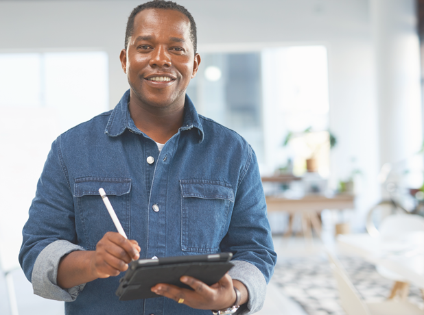 Happy middle-aged African American man writing on touchscreen tablet in office environment.