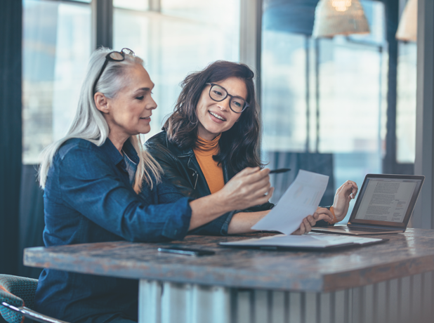 Two mixed-race female executives at work in the office discussing some paperwork.