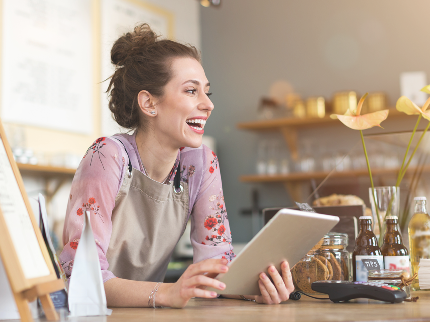 Female shopkeeper smiling while using a digital tablet on shop counter.