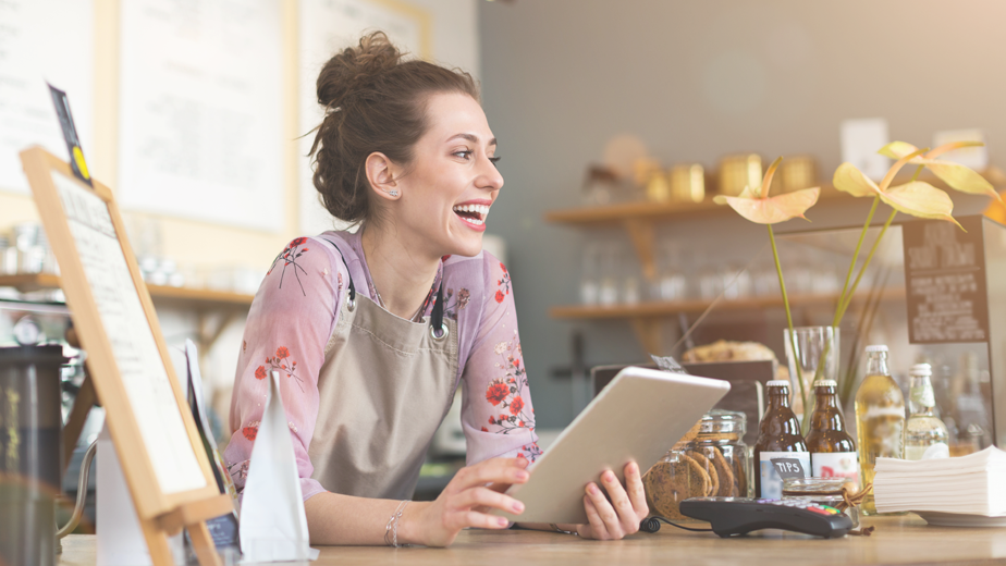 Female shopkeeper smiling while using a digital tablet on shop counter.