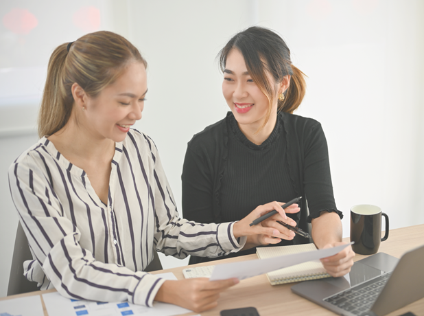 An image of two women having a consultation at a desk with coffee and a laptop.