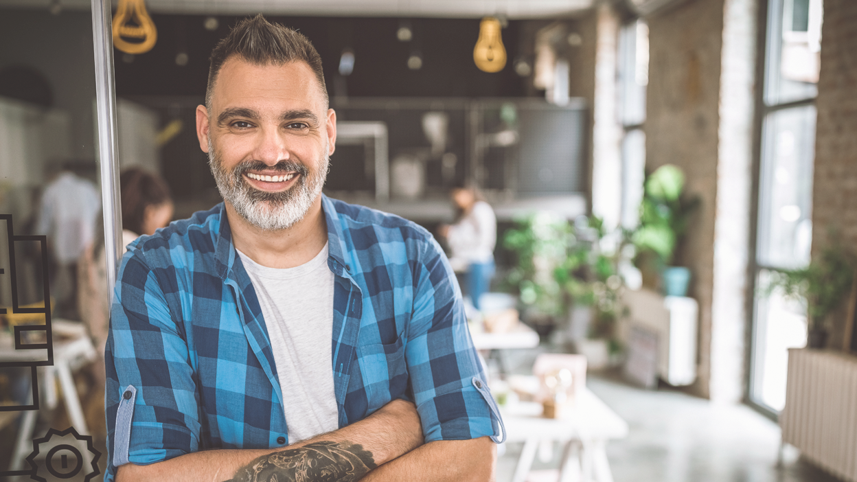 Middle eastern mid age man in a casual office setting looking at the camera and smiling.