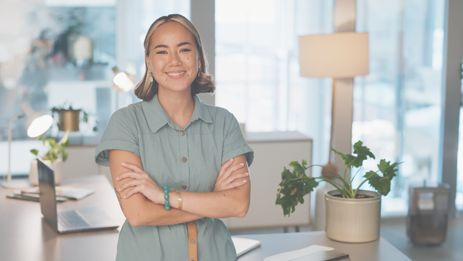 A young lady in a casual office environment smiling and looking at the camera.