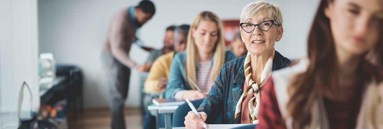 Mature female student taking notes while attending a course in lecture hall.