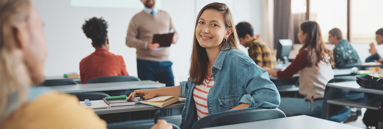 Adult female student, turning around and looking to camera smiling in a classroom environment.