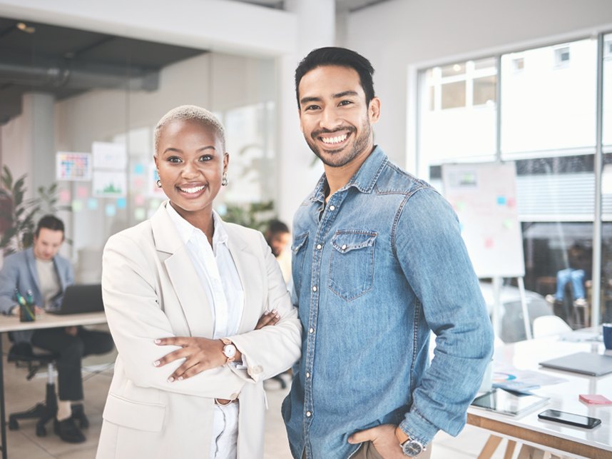 Portrait of two employees in a casual office setting looking at the camera and smiling.