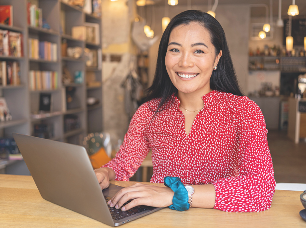 Asian woman sitting at a table in a library on her laptop.