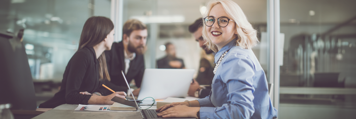 Business people discussing in the office with young blonde-haired woman looking to camera smiling.