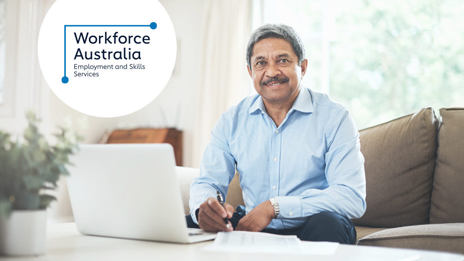 A senior man using a laptop at home while smiling to camera.