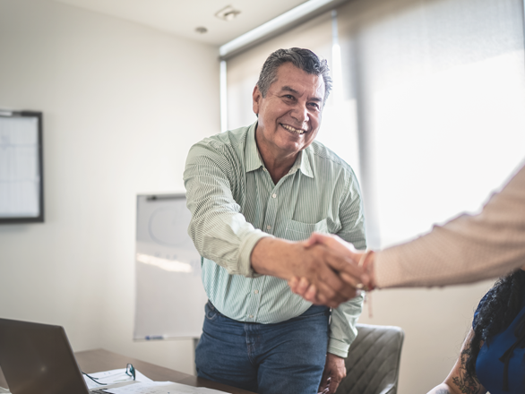 an older man standing up from his desk shaking someones hand.