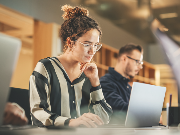 A woman wearing glasses looking at her laptop.