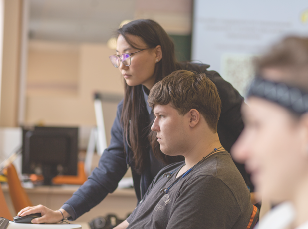 Teacher helping students on a computer in a classroom setting. 