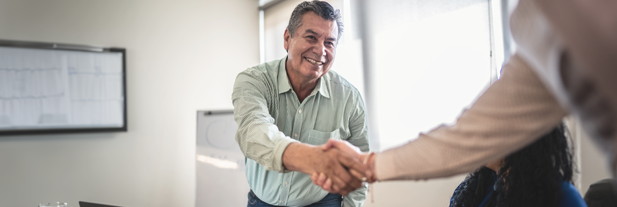 an older man standing up from his desk shaking someones hand.