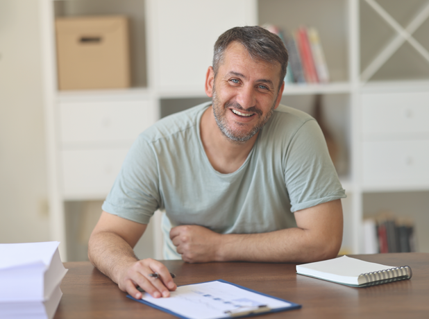 Business man working at filling out documents at desk, looking at the camera and smiling.