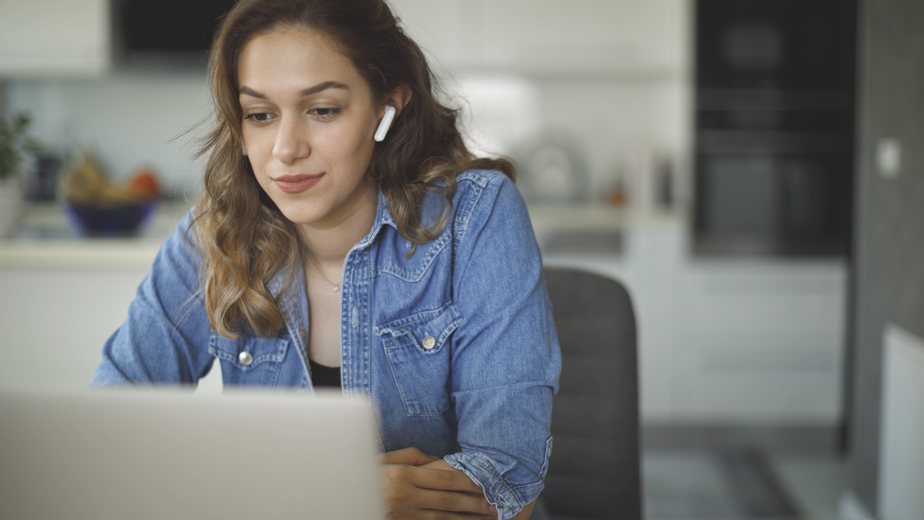 Smiling young woman with bluetooth headphones attends an online course at home