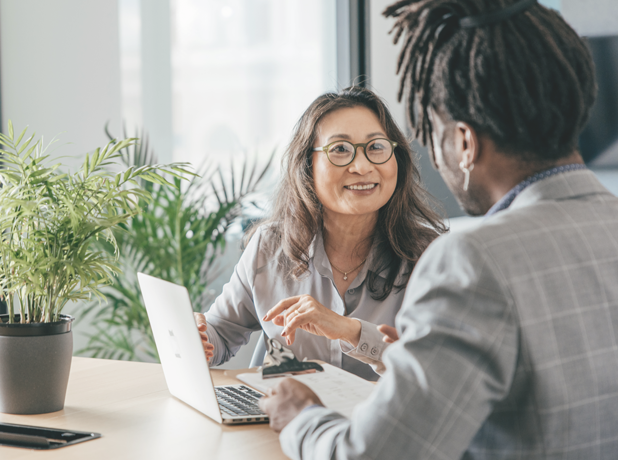 Two multicultural people sitting at desk having a one on one conversation about business. 