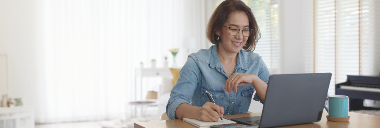 Asia happy female adult at desk looking at laptop while writing and working on her small business.