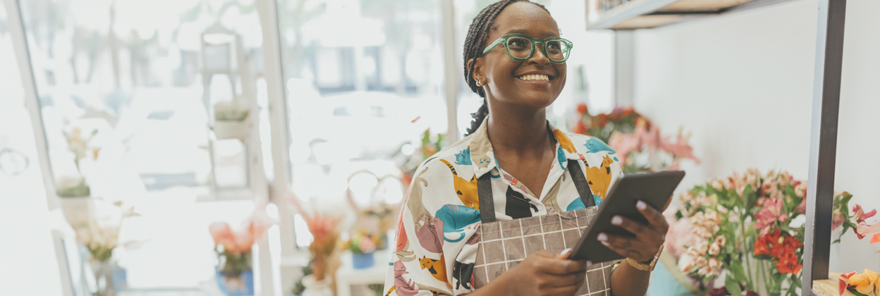 A 27-year-old African-American female entrepreneur owns a fresh flower shop, using a digital tablet. Stock