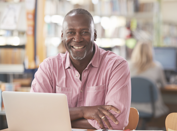 Portrait of bald, African Aerican mature male using laptop In Library