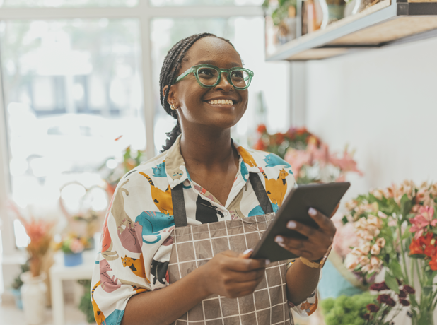 A 27-year-old African-American female entrepreneur owns a fresh flower shop, using a digital tablet. Stock