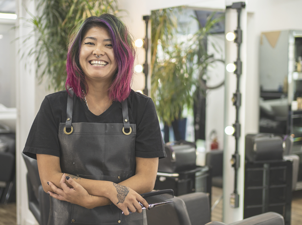 Portrait of Asain female hairdresser with pink dyed hair at hair salon holding scissors.