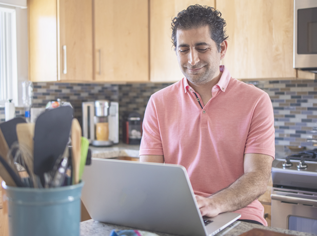 Mature man looking at laptop working from home kitchen