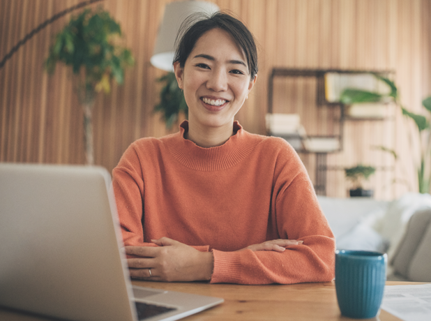 Young asian woman sitting in front of laptop smiling at camera