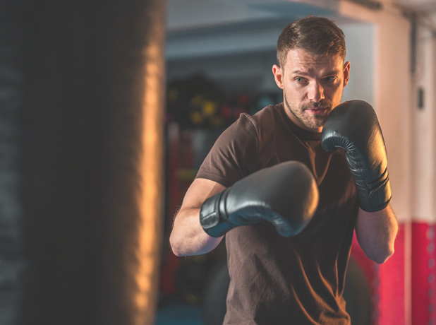 A young man in an exercise boxing class. He is wearing a brown T-shirt and boxing gloves.