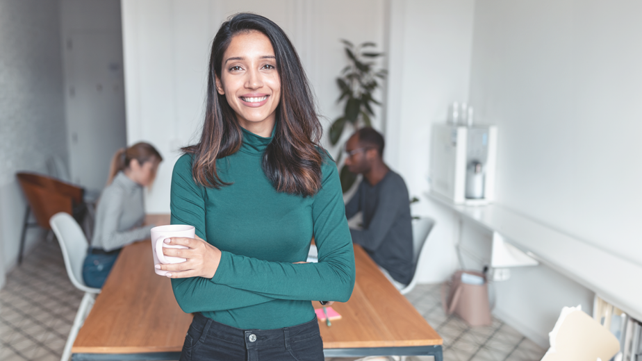 Shot of young indian business woman entrepreneur looking at camera in the office. In the background, her colleagues working.