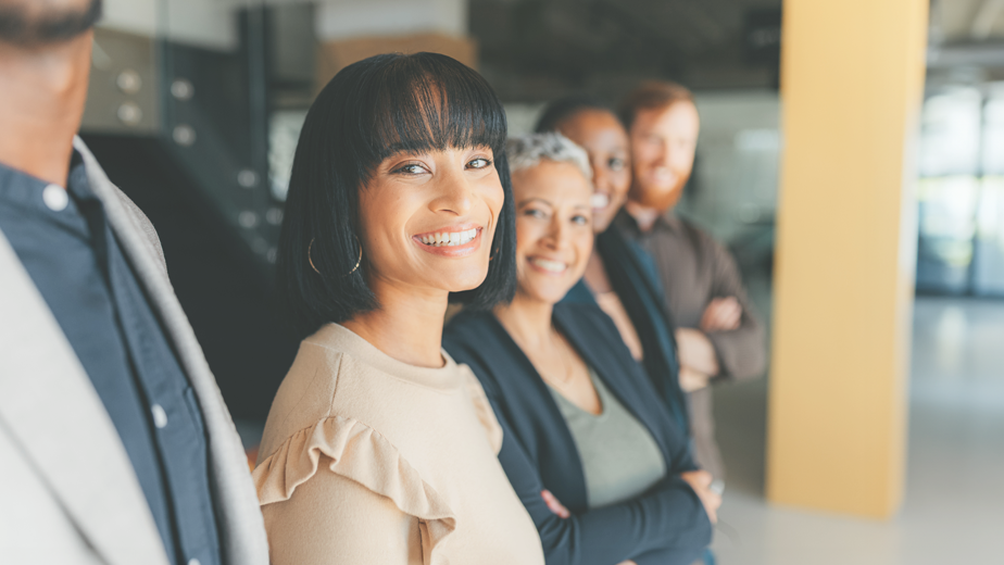 A team of employers line up in a row in an office building. Closest female looking to camera smiling. 