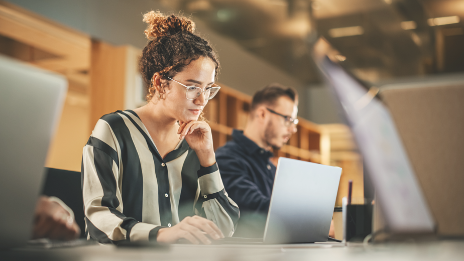 Portrait of Enthusiastic Hispanic Young Woman Working on Computer in a Modern Bright classroom