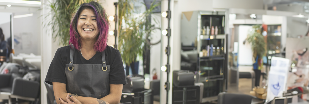 Portrait of Asain female hairdresser with pink dyed hair at hair salon holding scissors.