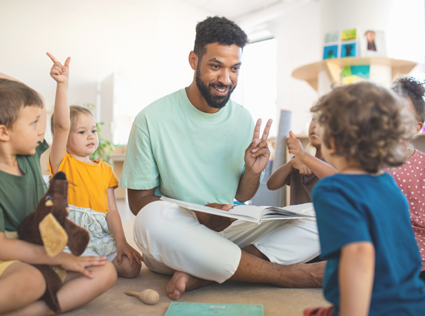 Group of small nursery school children with man teacher sitting on floor indoors in classroom, having lesson