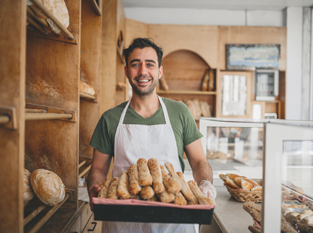 Male baker holding a basket of fresh bread in his bakery business.