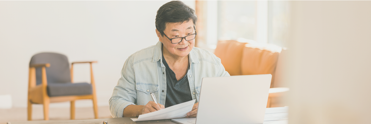 Cheerful mature-aged Asian businesswoman works on financial statements at home.<br />
